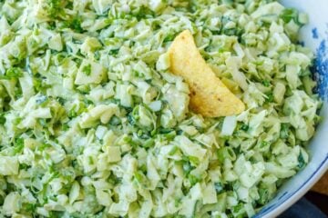 A corn chip dipped into a bowl of Green Goddess Salad in a white bowl