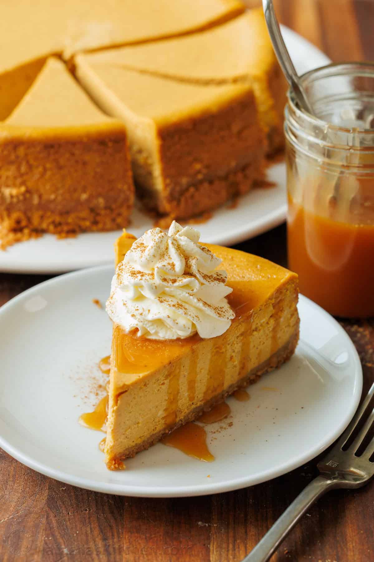 My pumpkin cheesecake recipe is so easy to make and is better than any professional baker! Save money and make your Holiday dessert at home! Pumpkin Cheesecake cut into pieces with one slice on a plate with caramel sauce drizzled on top