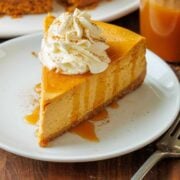 Slice of pumpkin cheesecake on a white plate with caramel drizzle and whipped cream