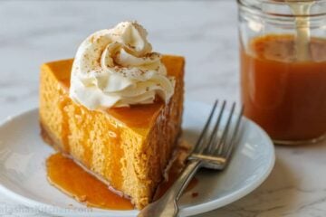 Pumpkin cheesecake slice on a plate with fork and homemade caramel sauce to drizzle on top.