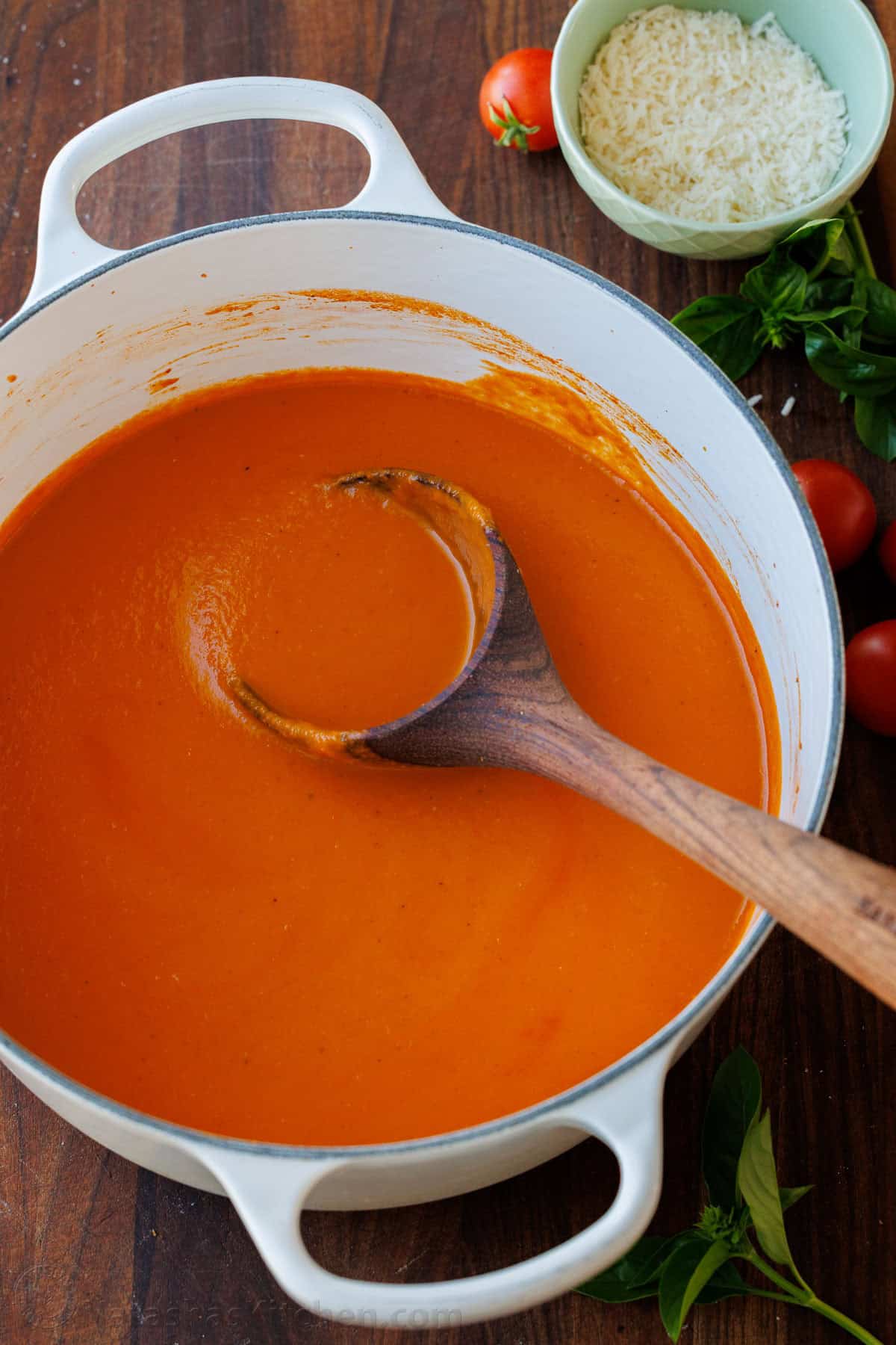 Roasted tomato soup has layers of delicious flavor for a creamy satisfying and easy dish. Pair with Grilled Cheese for the best Fall recipe. Red broth in a white Dutch Oven with a wooden spoon