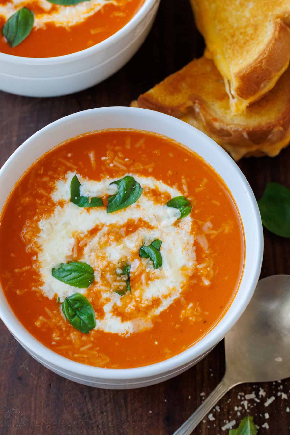 Roasted tomato soup has layers of delicious flavor for a creamy satisfying and easy dish. Pair with Grilled Cheese for the best Fall recipe. Roasted Tomato soup with Parmesan cheese and basil in a white bowl