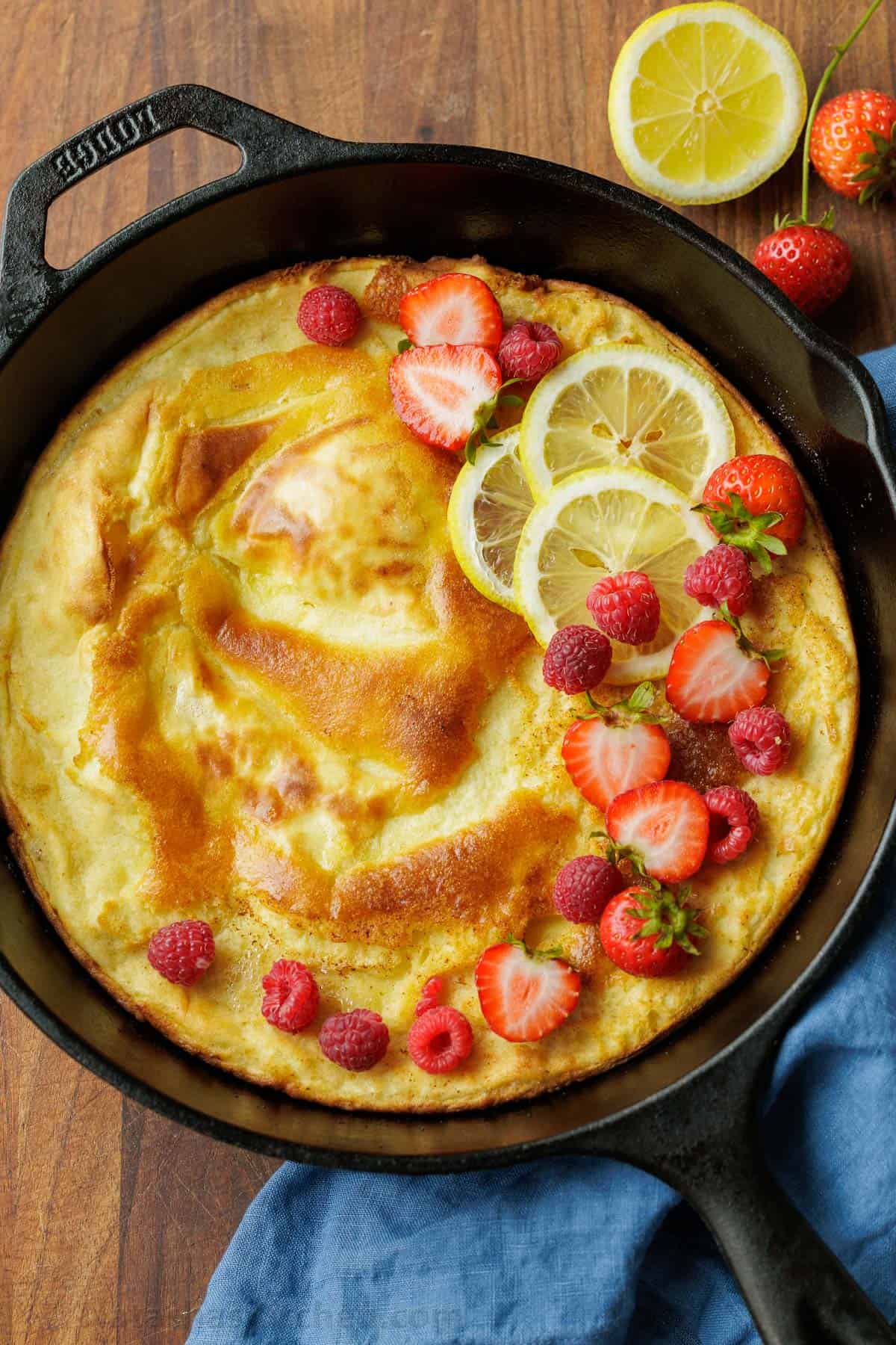 Easy Sourdough Dutch Baby pancake recipe using sourdough discard. Blend or whisk the batter, and it cooks up puffy and golden in the oven. Sourdough Dutch Baby pancake recipe in a cast iron pan topped with lemon slices and sliced strawberries