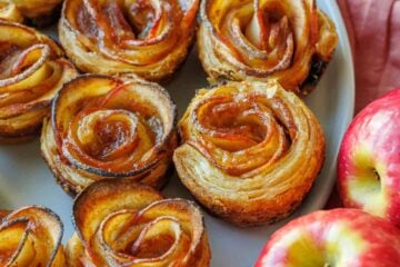 Apple roses lined up on a plate with two apples