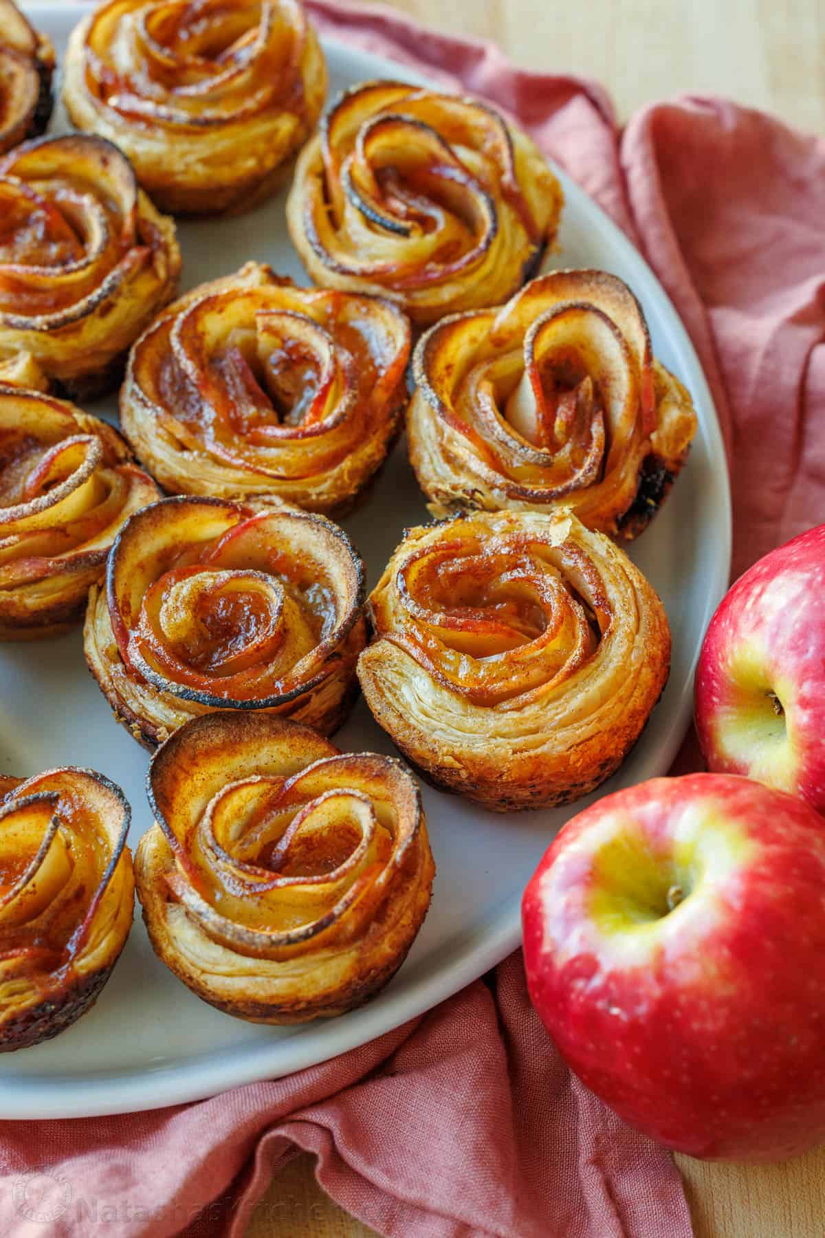 Apple roses lined up on a plate with two apples