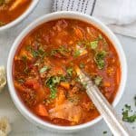 Cabbage soup recipe in a bowl with parsley garnish and a large metal spoon