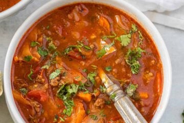 Cabbage soup in a white bowl with a spoon and white tablecloth