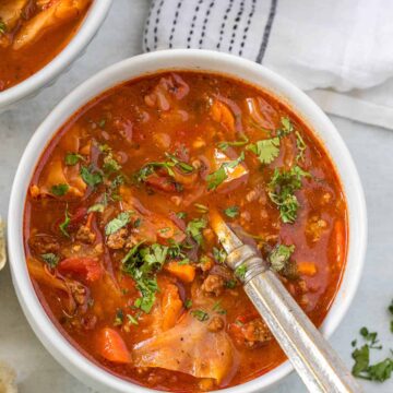 Cabbage soup in a white bowl with a spoon and white tablecloth