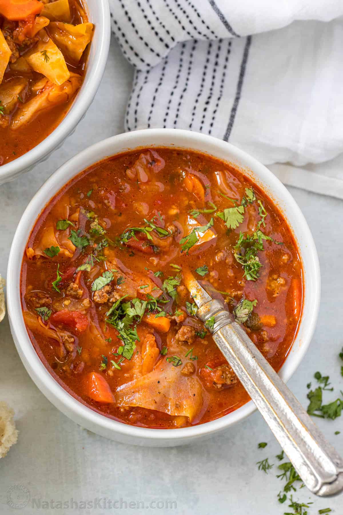 My homemade Cabbage Soup recipe is so easy to make and tastes as good as my Cabbage rolls without the hassle! Filling & Freezer-friendly. Cabbage soup in a white bowl with a spoon and white tablecloth