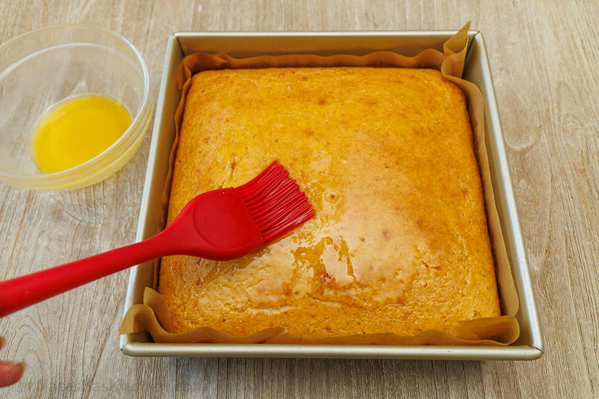 The best homemade cornbread recipe is easy to make with pantry staples. Serve with your favorite holiday or BBQ menu and honey butter on top. brushing honey butter of a pan of the best homemade cornbread recipe in a 9x9 pan
