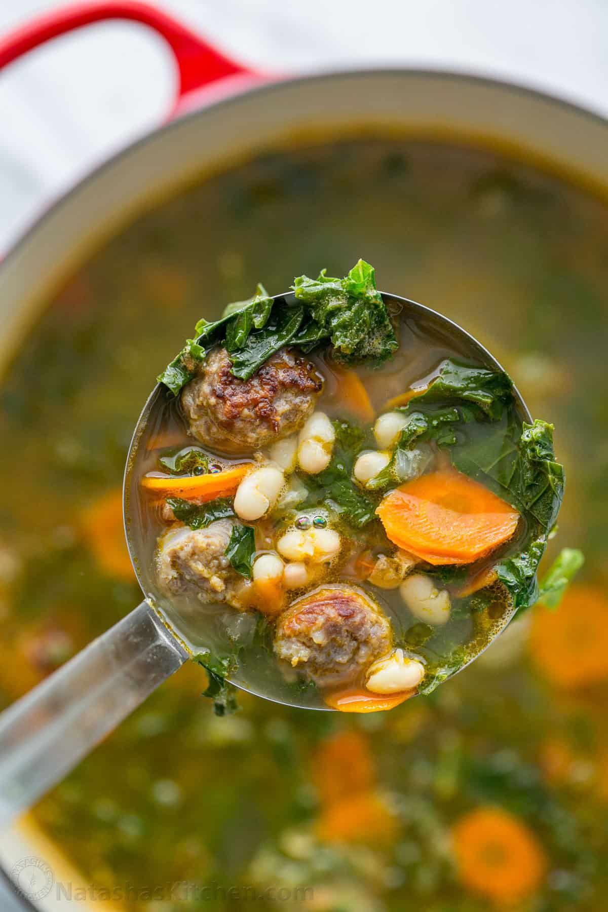 Sausage and Kale Soup is full of veggies and hearty bratwurst sausage cut like meatballs, and it's easy to make in 1 pot and in under 1 hour. Soup ladle with sausage, white beans, sauce, kale and carrot soup over a Dutch oven.