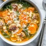 Bowl of Sausage and Kale Soup recipe in a white bowl with slices of carrot and parmesan cheese on top