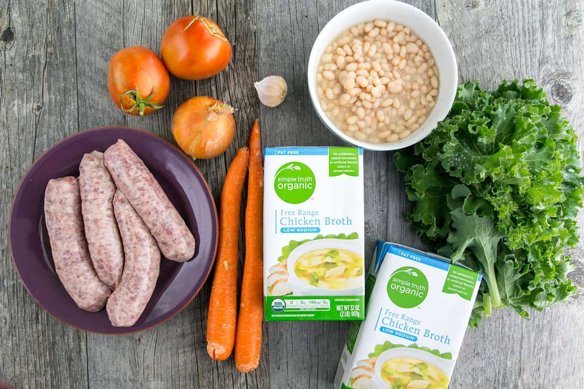 Sausage and Kale Soup is full of veggies and hearty bratwurst sausage cut like meatballs, and it's easy to make in 1 pot and in under 1 hour. Ingredients for hearty Fall recipe including bratwurst, tomatoes, onion, carrots, chicken broth, white beans, and greens