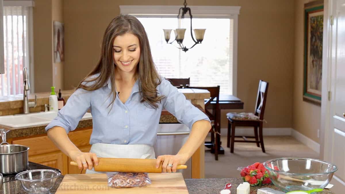 Easy Strawberry Pretzel Salad is a crowd-favorite dessert recipe at parties and picnics! Easy make-ahead directions everyone will love! Natasha showing how to crush pretzels for Strawberry Pretzel Salad using a rolling pin