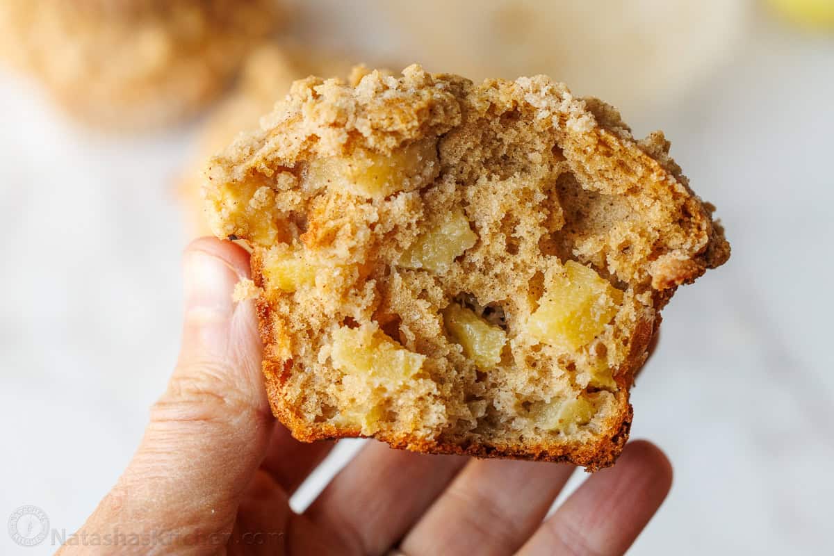 Bakery-style Apple muffins with crumb topping are so easy to make, with a moist crumb and chunks of apple inside. Uses just pantry staples. a hand holding half of a soft apple muffin with chunks of apples inside.