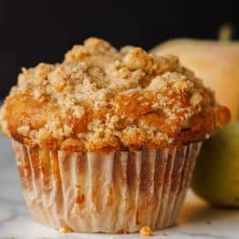 Apple muffin with crumb topping on a table with a white muffin wrapper