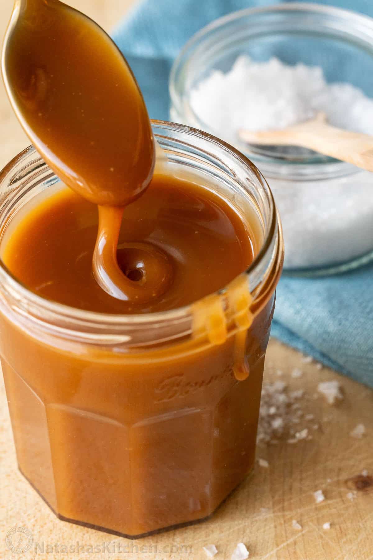 Drizzling caramel topping into a jar with sea salt in the background