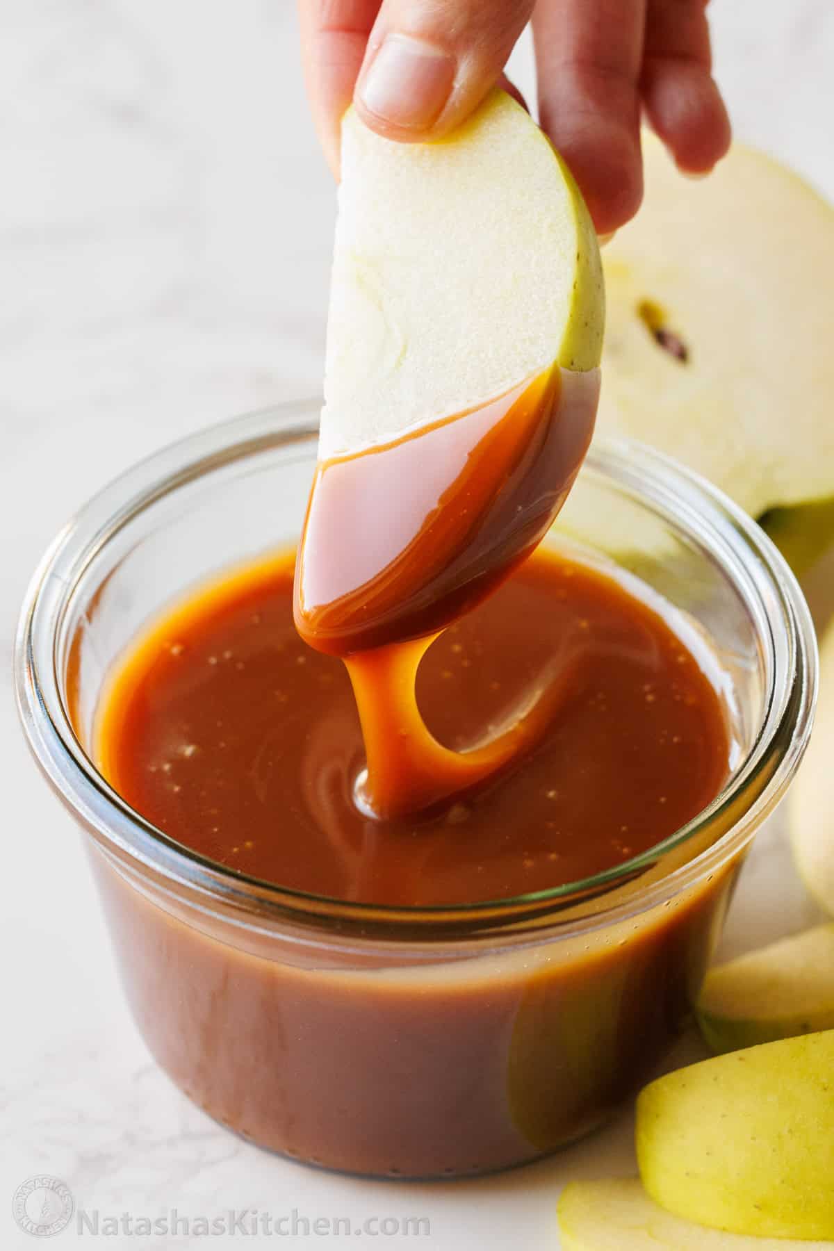 Apple slice dipped in homemade caramel sauce in a glass jar