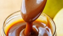 Spoon drizzling dark brown caramel sauce from scratch into a mason jar