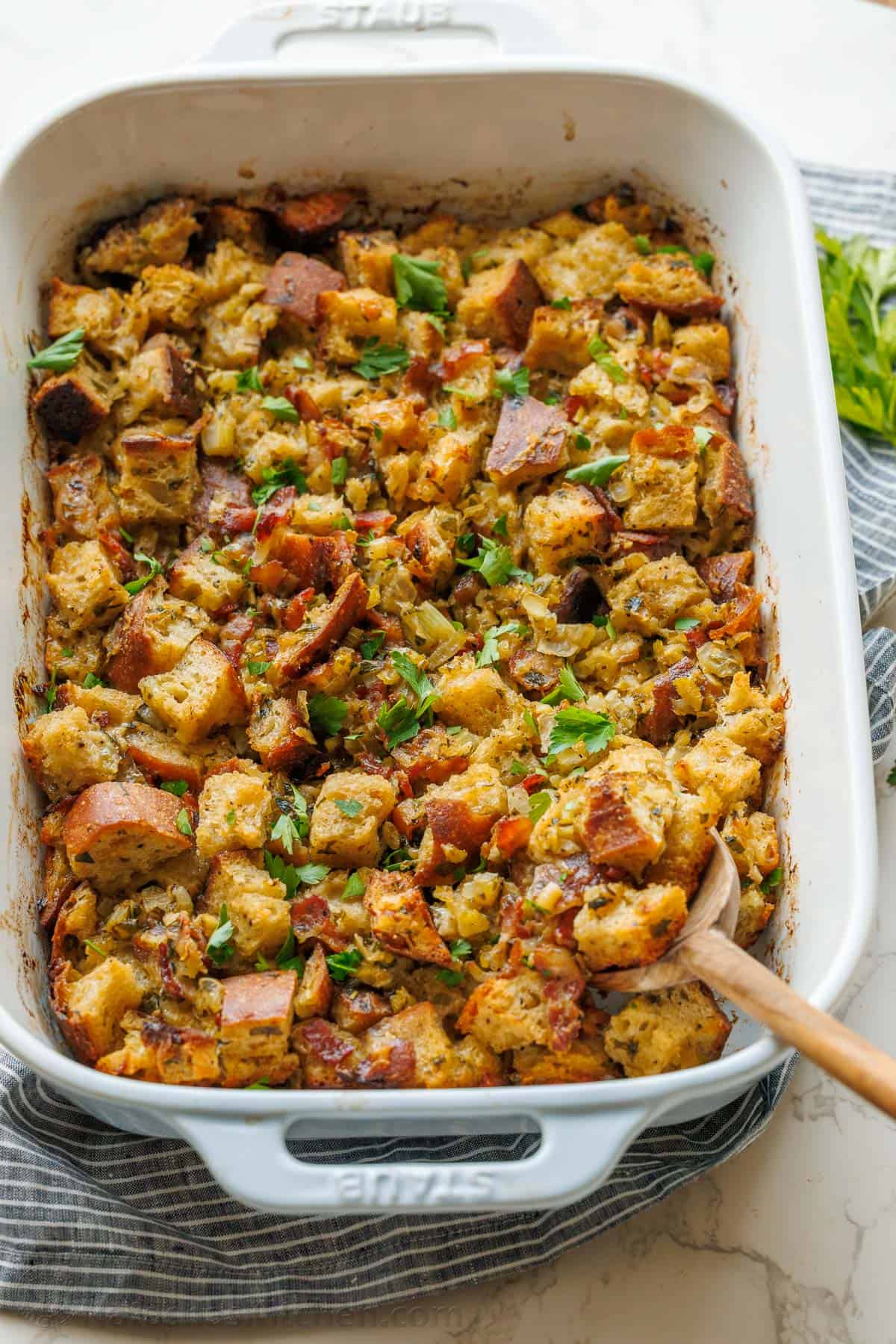 best stuffing recipe for thanksgiving in a white casserole dish with a wood spoon to serve