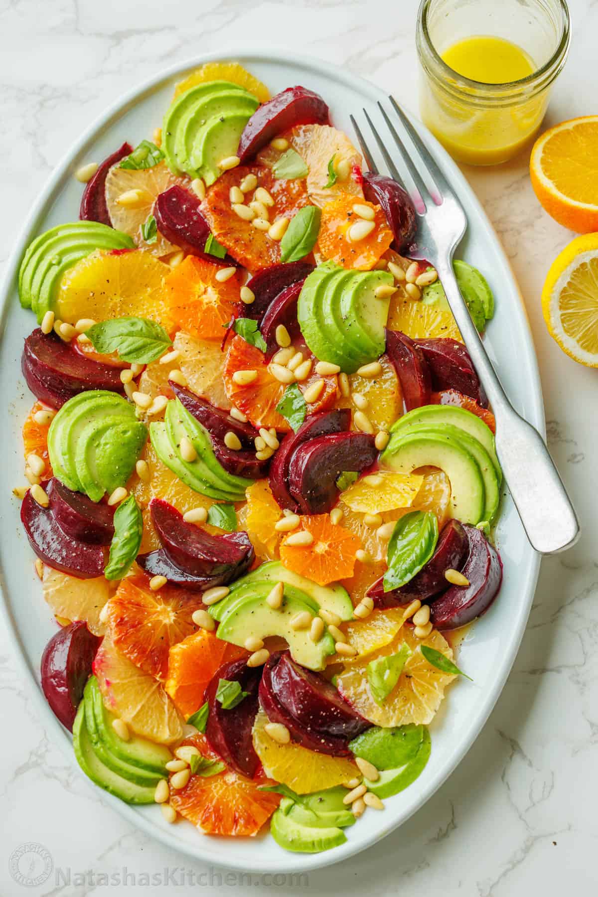 Citrus salad on a white plate with a fork and lemon vinaigrette in a mason jar