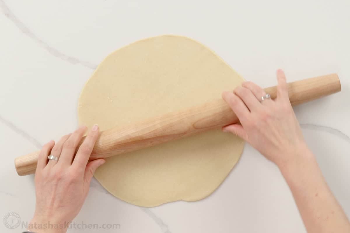 hands rolling dough using a wooden rolling pin