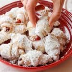 Rugelach covered in powdered sugar on red plate