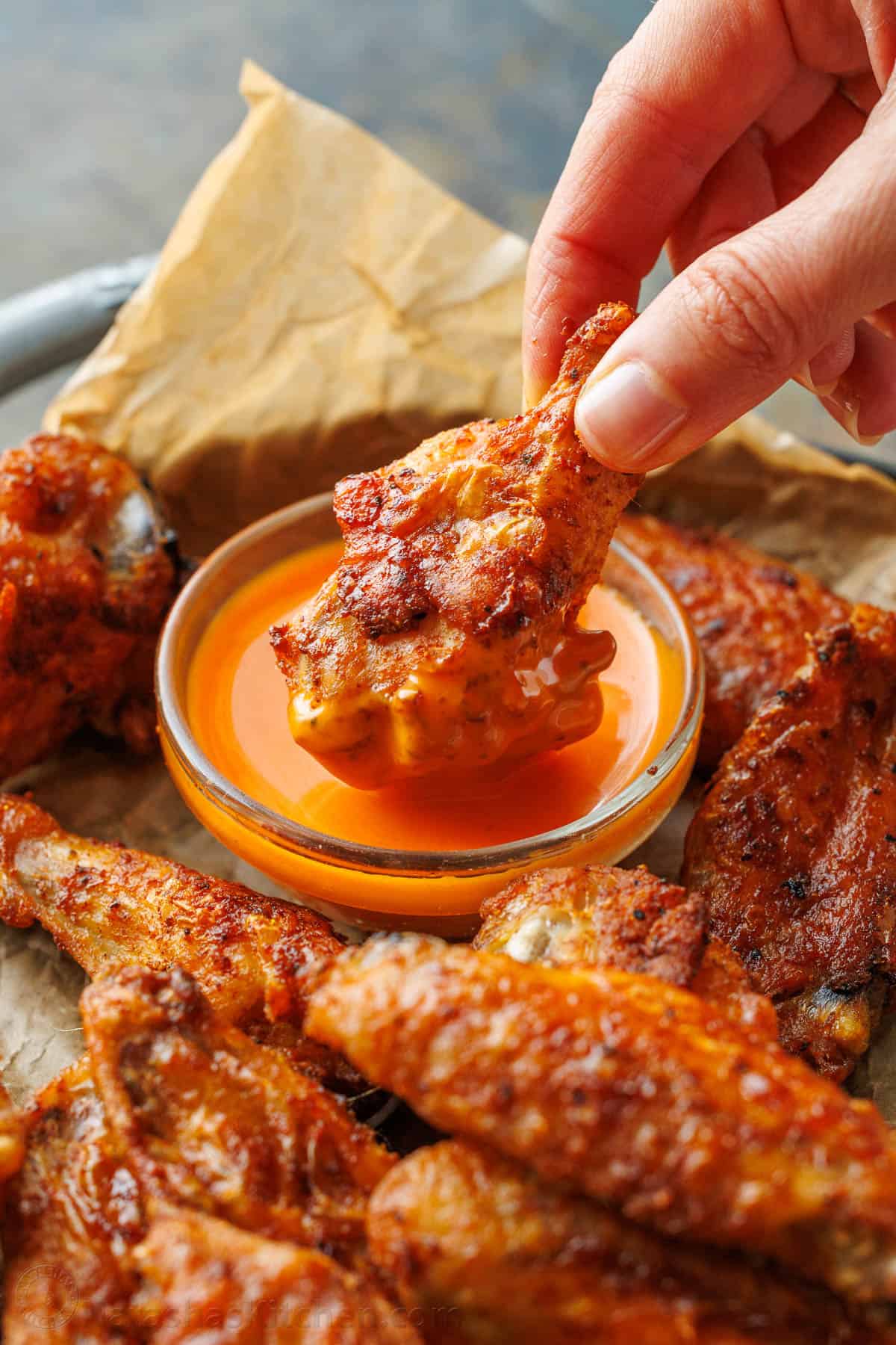Crispy baked chicken wings dipped into buffalo sauce in a bowl