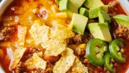 Easy taco soup recipe in a white bowl with cheese, chips and avocado chunks