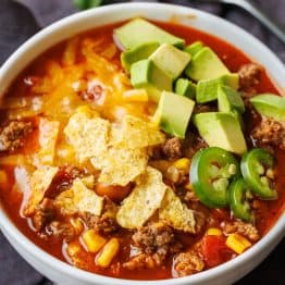 Easy taco soup recipe in a white bowl with cheese, chips and avocado chunks