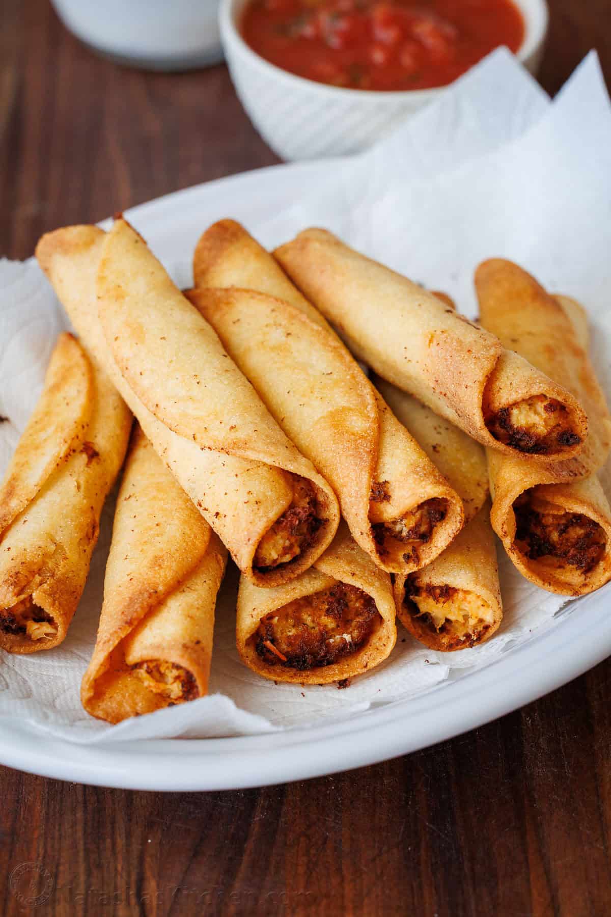 homemade chicken taquitos on a white plate with salsa for serving