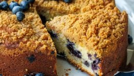 slice cut out of a whole blueberry coffee cake with fresh blueberries on top