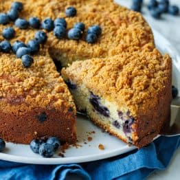 slice cut out of a whole blueberry coffee cake with fresh blueberries on top