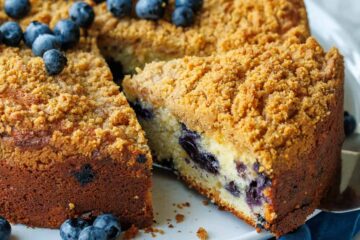 slice cut out of a whole blueberry coffee cake with fresh blueberries on top