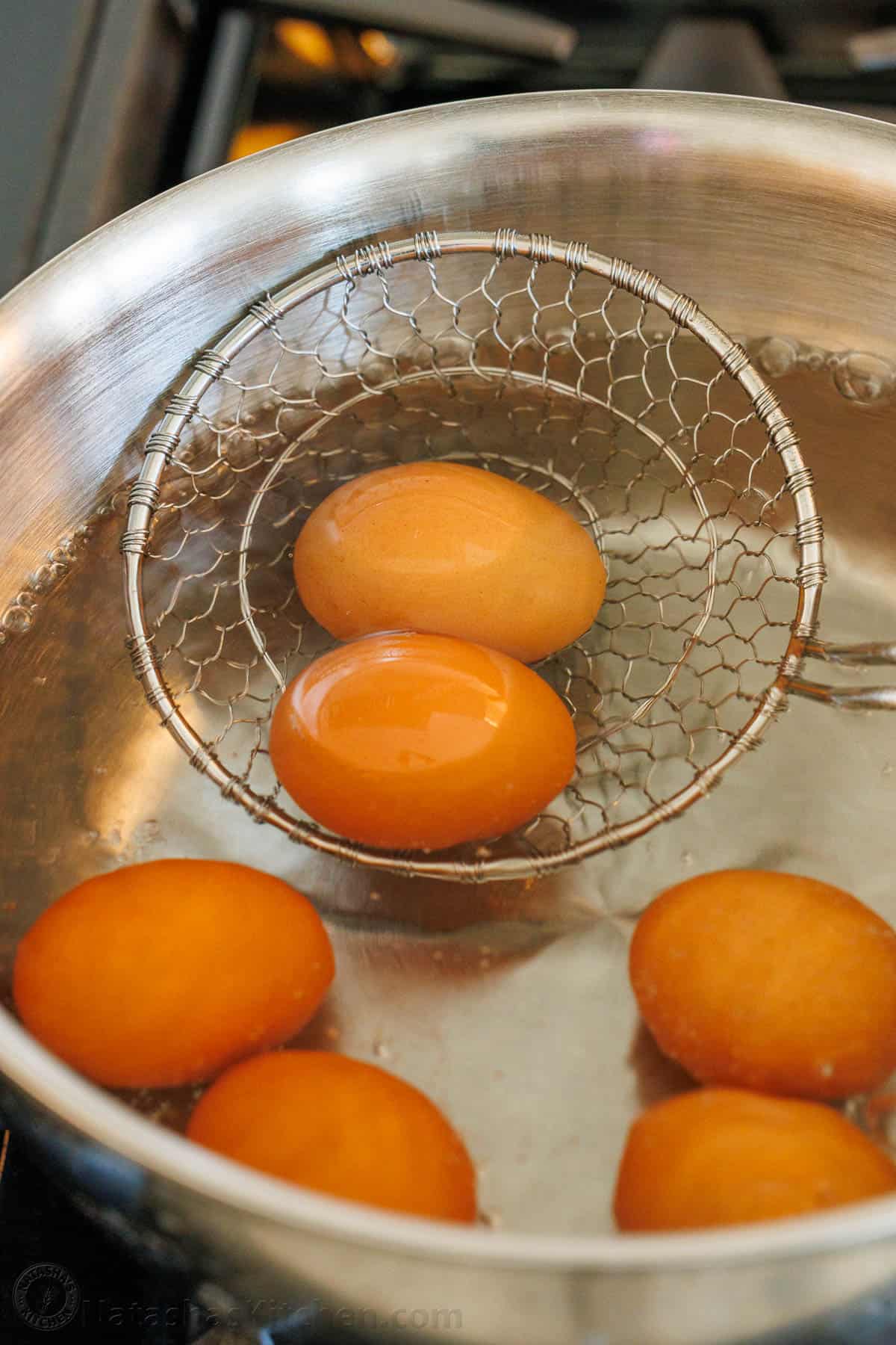 strainer removing brown eggs from a pot of water