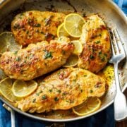 Lemon pepper chicken recipe in a skillet with lemon slices and lemon butter sauce and parsley to garnish