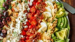 Large Greek Cobb Salad on a white plate with greek dressing in a mason jar