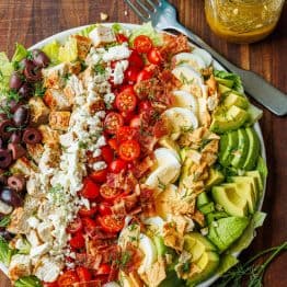 Large Greek Cobb Salad on a white plate with greek dressing in a mason jar