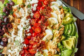 Large Greek Cobb Salad on a white plate with greek dressing in a mason jar