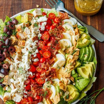 Large Greek Cobb Salad on a white plate with greek dressing in a mason jar
