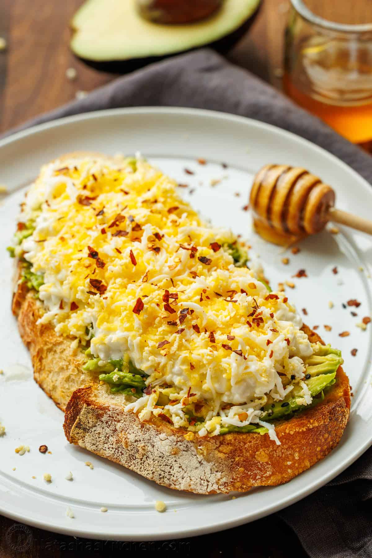 High Protein Avocado Toast with cottage cheese, avocado, grated egg, honey, and chili flakes. A filling breakfast with 23 grams of protein. High protein avocado toast with egg and cottage cheese on sourdough bread