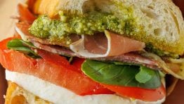 Homemade Italian sub sandwich with a slice of tomato, fresh mozzarella cheese, basil, pesto, meat and toasted bread