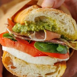 Homemade Italian sub sandwich with a slice of tomato, fresh mozzarella cheese, basil, pesto, meat and toasted bread