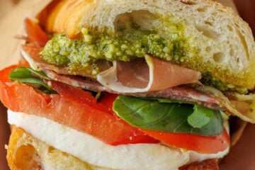 Homemade Italian sub sandwich with a slice of tomato, fresh mozzarella cheese, basil, pesto, meat and toasted bread