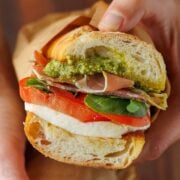Italian sandwich recipe with layers of mozzarella, deli meat, pesto, and fresh tomato with basil