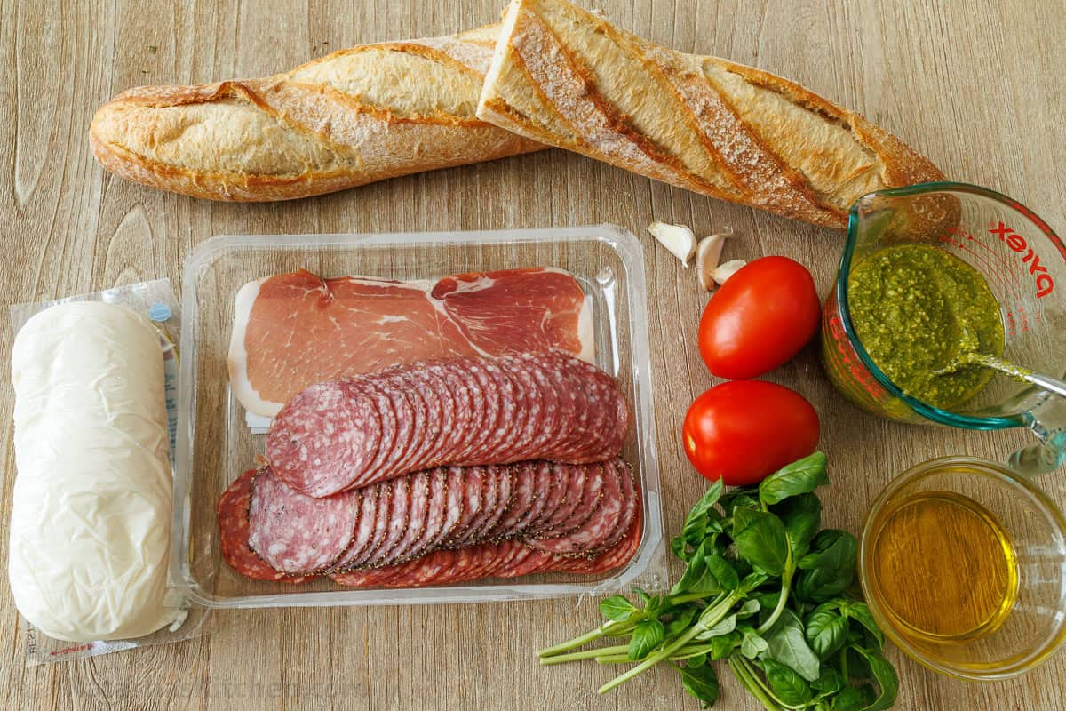 Ingredients for authentic Italian sandwich with Italian deli meat, baguette, tomatoes, garlic, pesto and basil