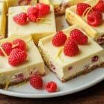 Easy raspberry lemon cheesecake bars on a plate with graham cracker crust and strawberries on top.