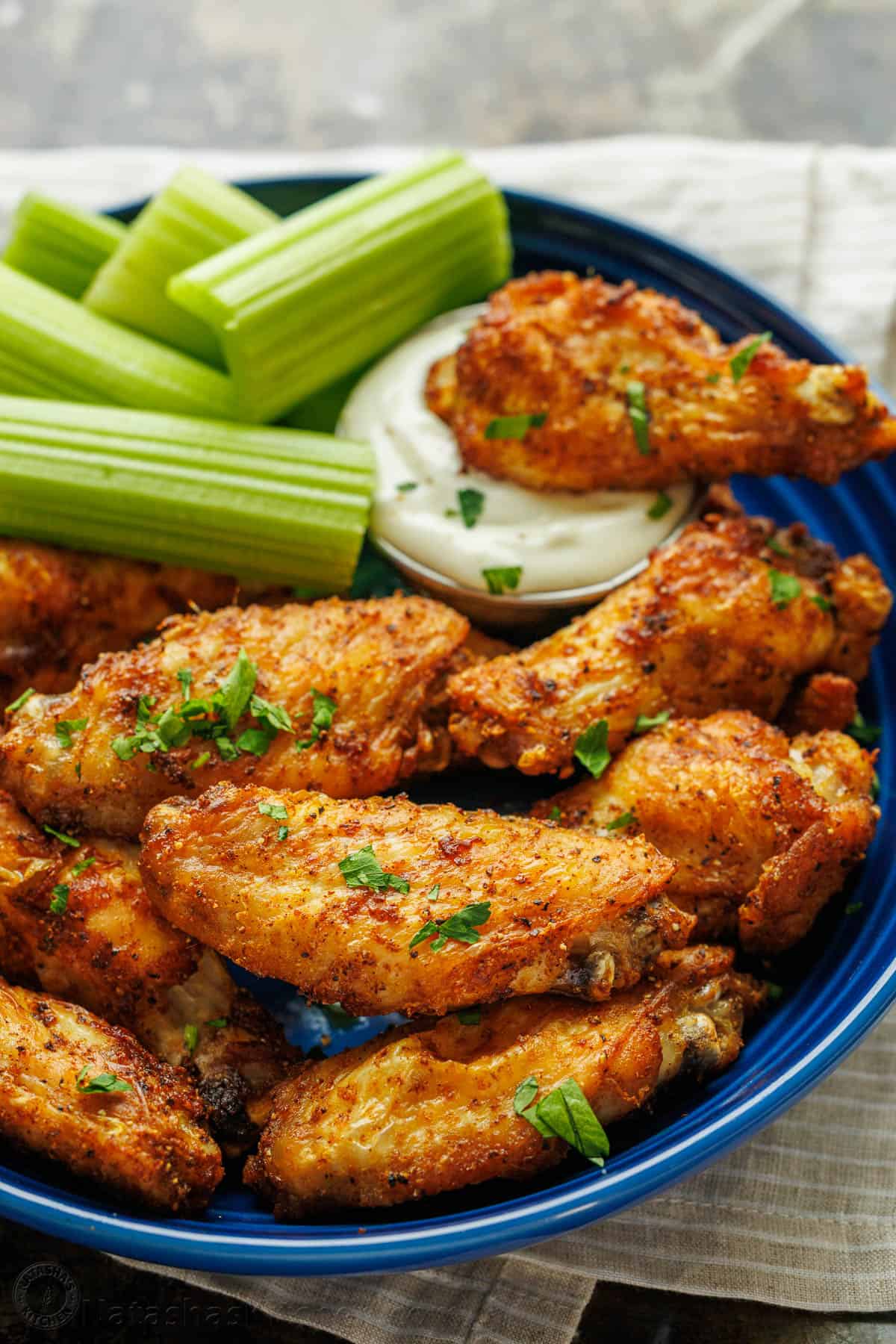 Air Fryer Chicken wings served in a blue plate with a wing dipped in sauce