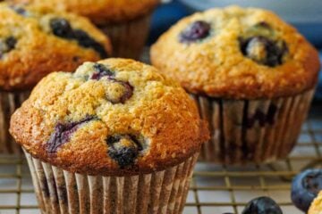 Blueberry banana muffins on a baking rack with fresh blueberries in a bowl