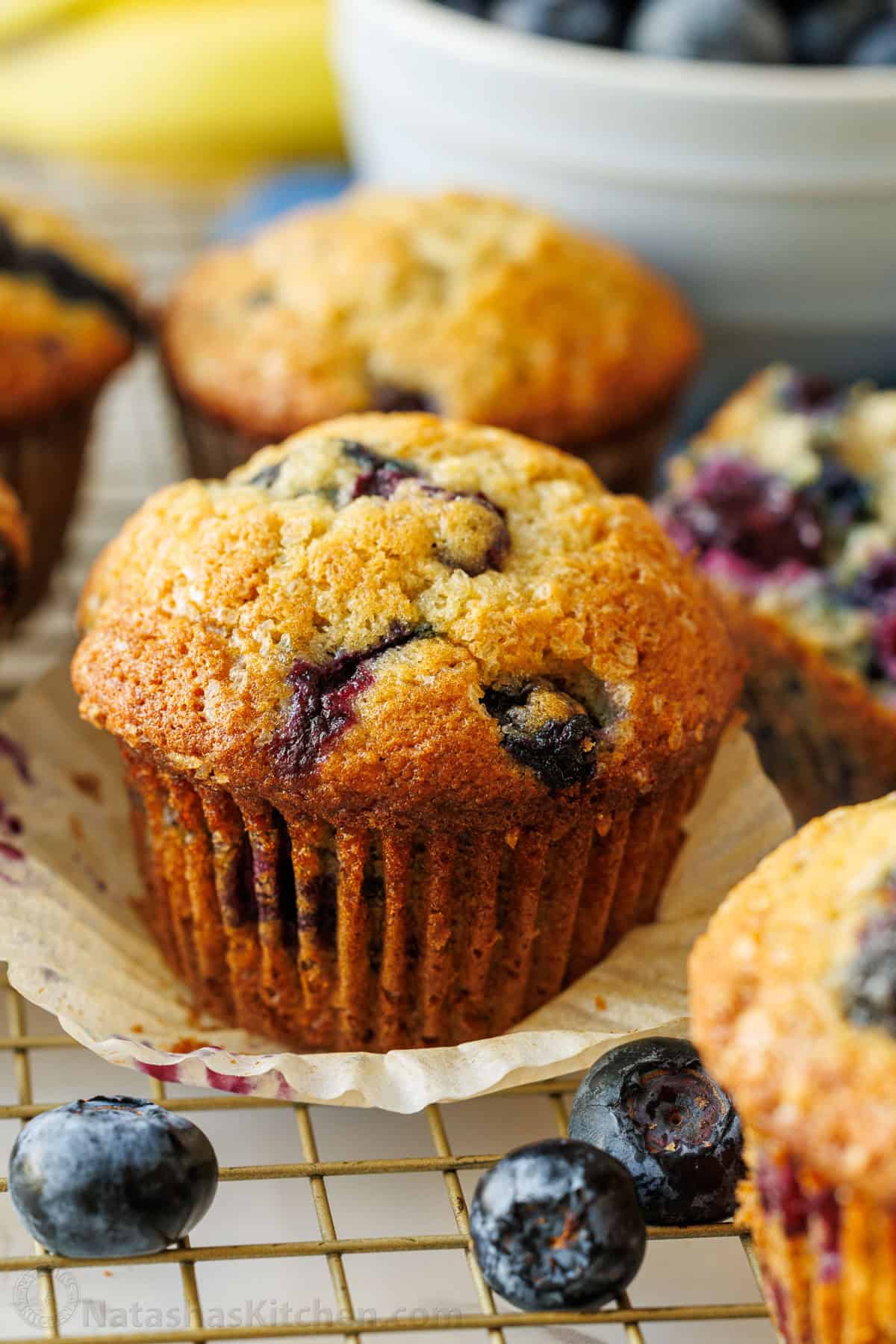 Easy Blueberry Banana Muffins bake up moist, tall, domed, and fluffy with great banana flavor and plenty of juicy blueberries. cupcake liner removed from cupcake with fresh berries and browned exterior